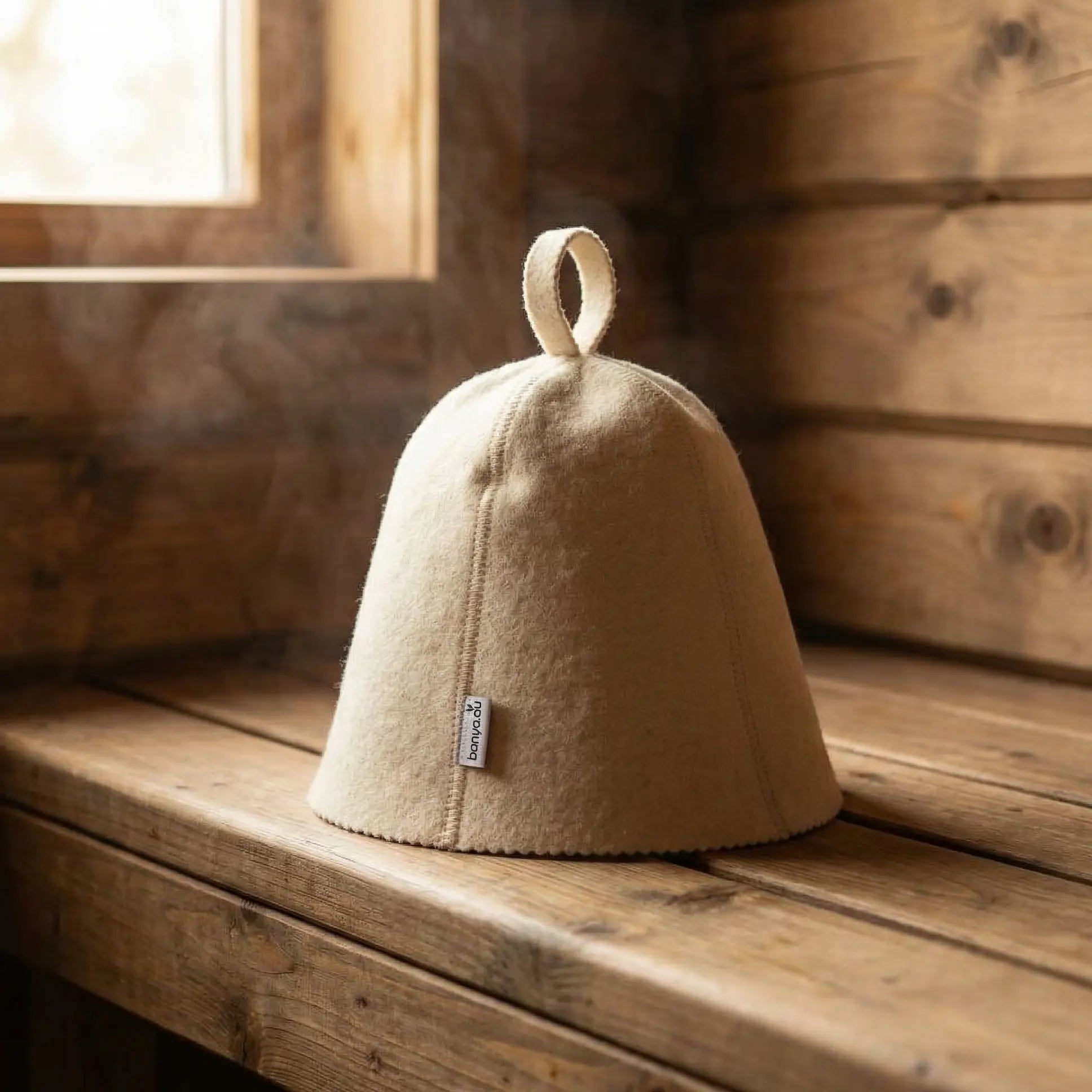 White 5mm natural wool sauna hat sitting on a wooden banya bench with steam in background