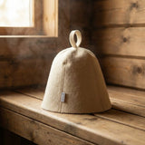 White 5mm natural wool sauna hat sitting on a wooden banya bench with steam in background