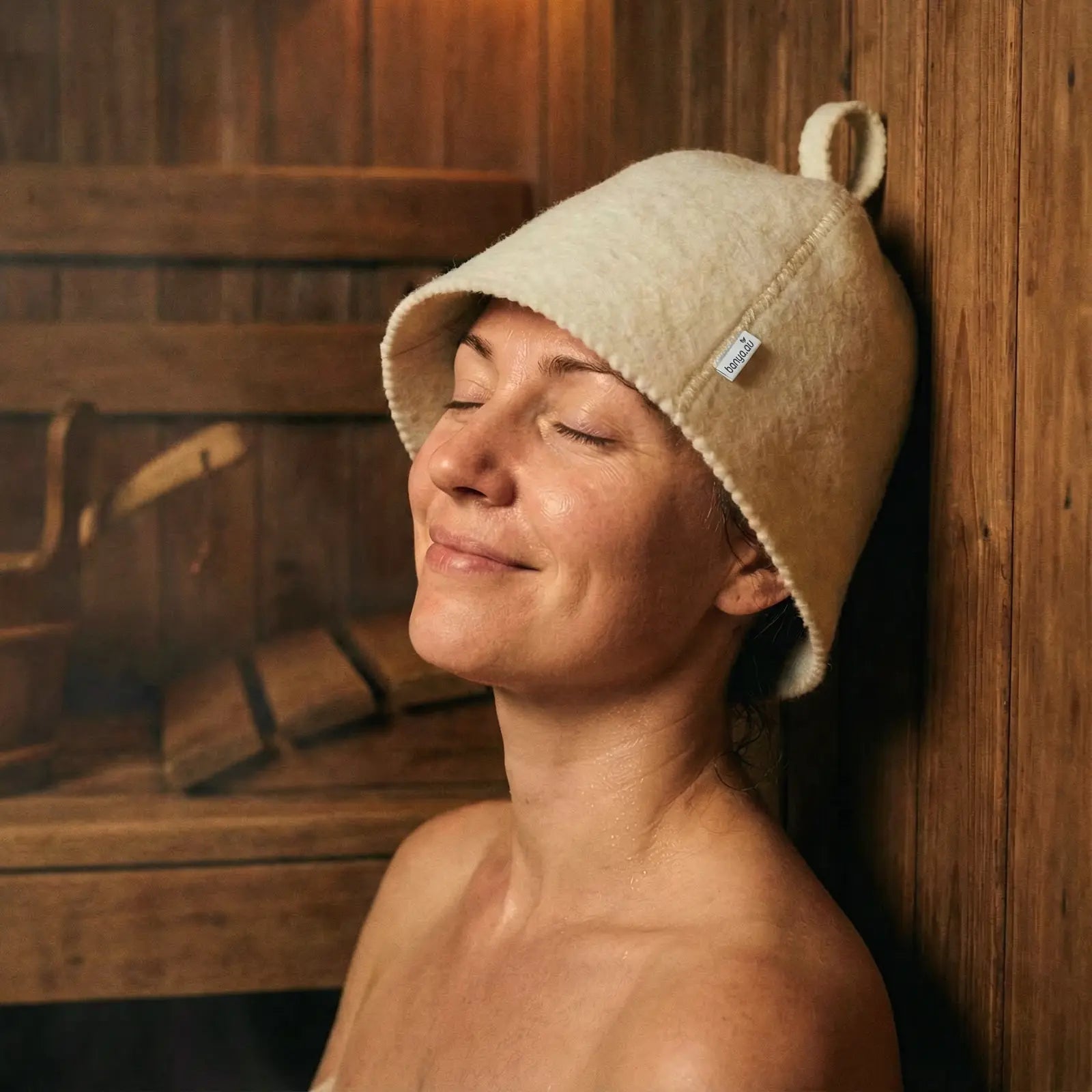 Woman wearing protective white wool sauna hat relaxing in a hot wooden sauna